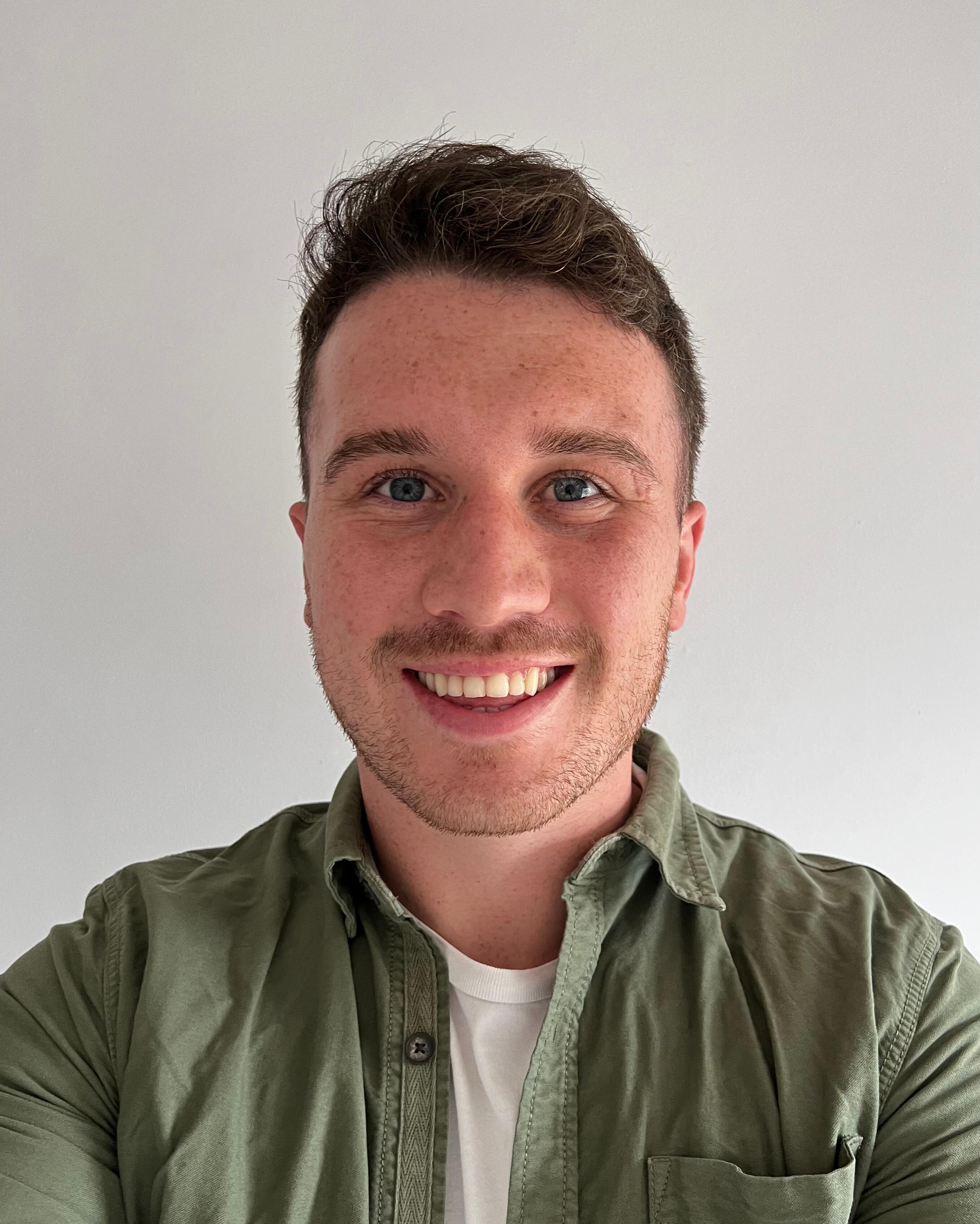 headshot photo of Owen, wearing a green shirt, smiling at the camera